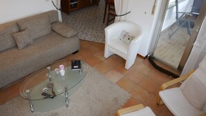Ett vardagsrum med en soffa, en vit fåtölj, ett soffbord i glas och en matplats i bakgrunden.