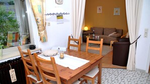 En matplats med ett träbord och stolar, ett fönster med gardiner, ett element och en soffa i bakgrunden.