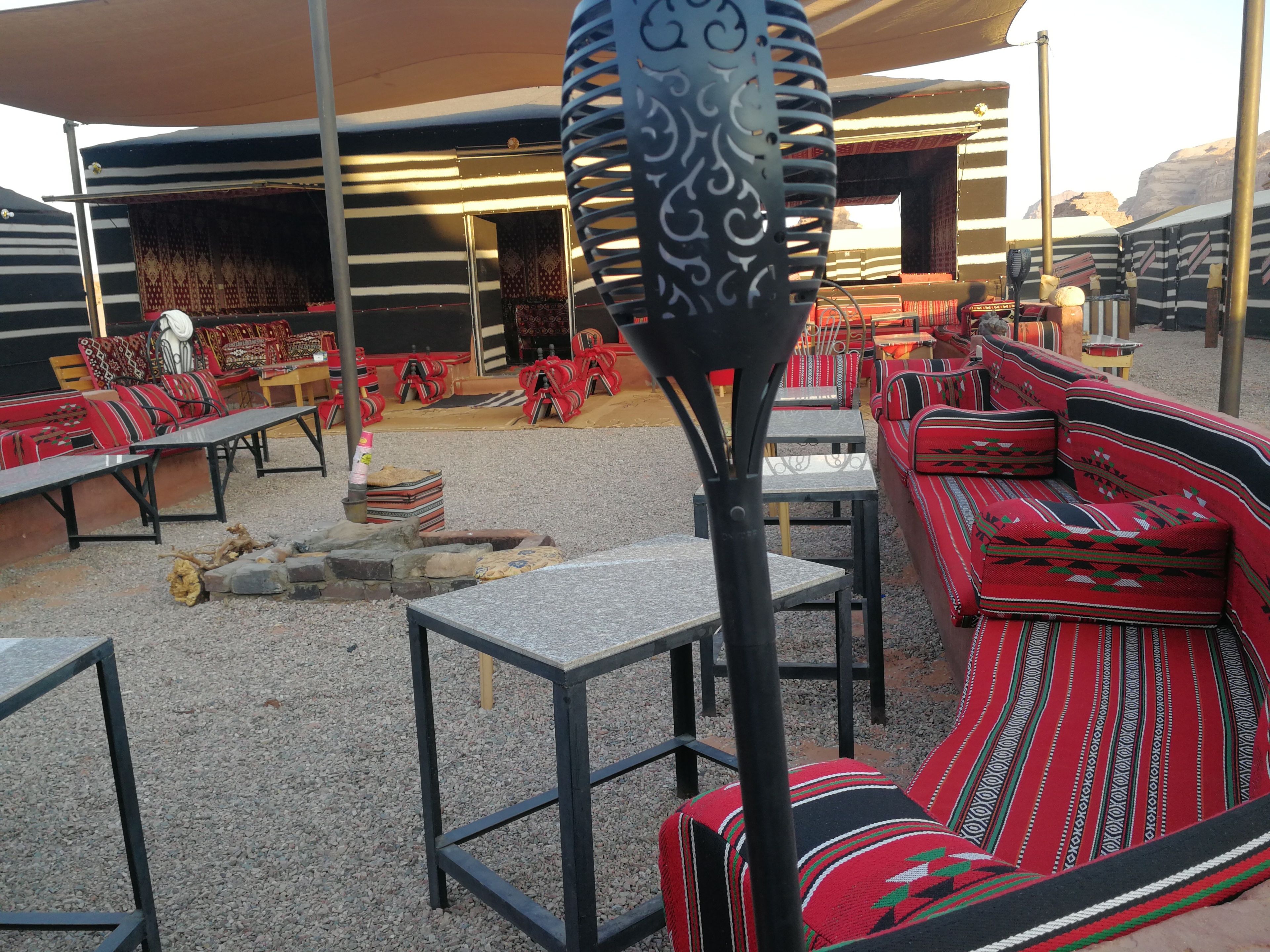 An outdoor seating area with striped cushions and tables, under a shaded structure.