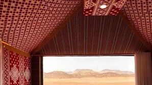 Habitación con un ventanal grande que ofrece vista al desierto, una cama y una cortina estampada.