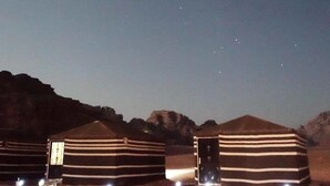 Varias yurtas a rayas con puertas abiertas, ubicadas en un paisaje desértico nocturno con estrellas visibles en el cielo.