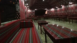 Un restaurante con paredes de rojo y blanco estampado, mesas y bancos de madera, y un techo con diseño.