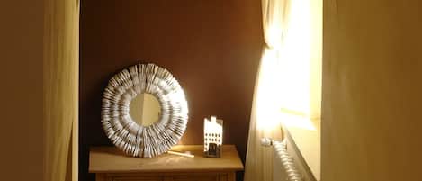 A room with a wooden vanity, a round mirror, and a small table with a lamp.