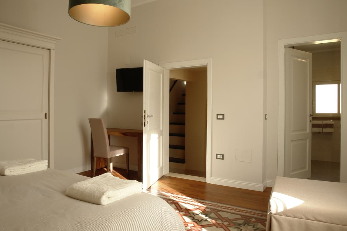 A hotel room with a bed, a desk, a chair, a television, and a staircase leading to another room.