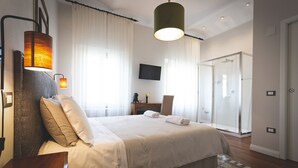 A modern hotel room with a large bed, a desk, a flat-screen TV, and a walk-in shower. - Piazza Duomo Deluxe (Cecina)