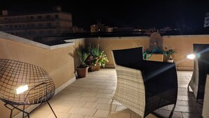 A rooftop terrace with a seating area, potted plants, and a view of the cityscape at night. - Piazza Duomo Deluxe (Cecina)