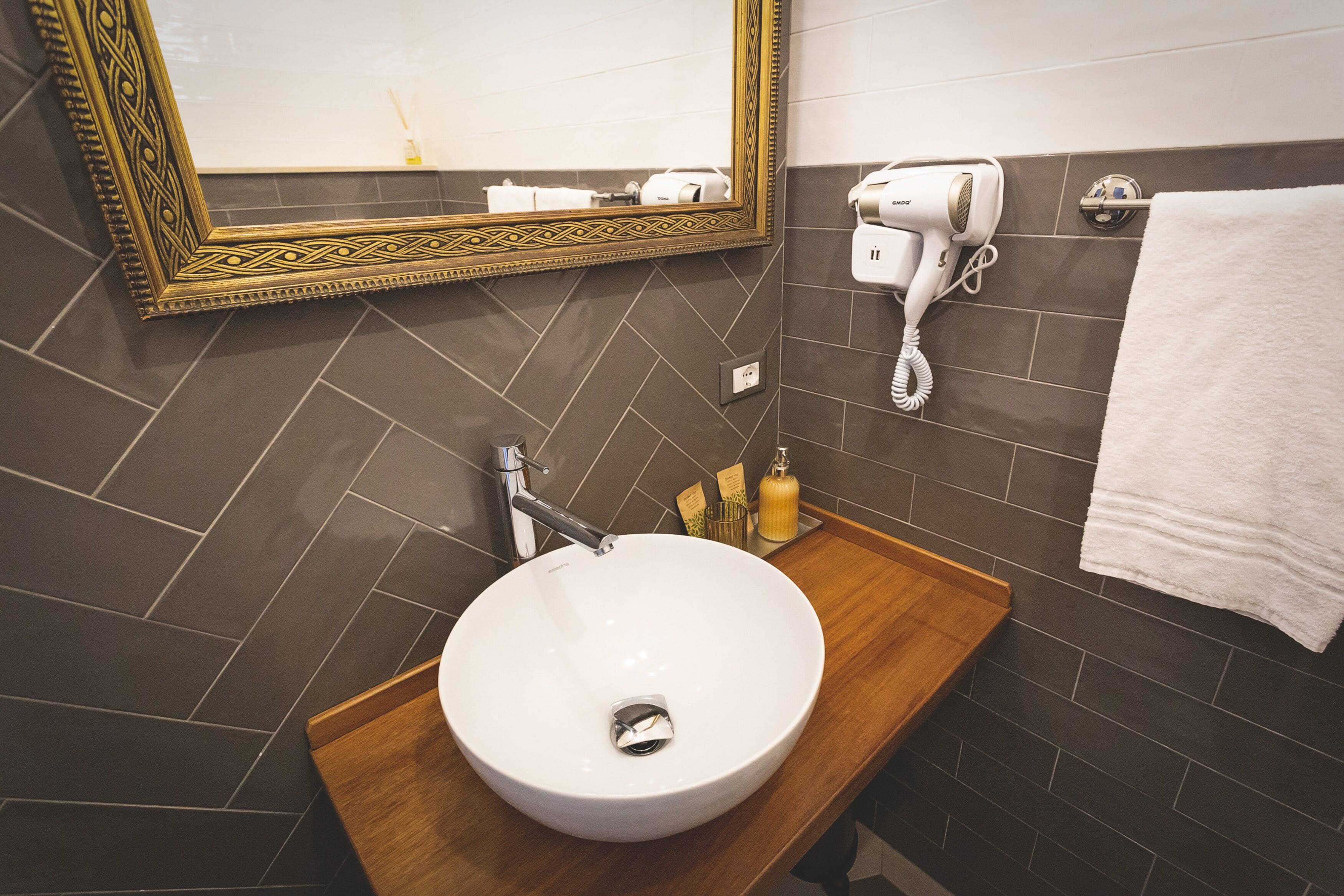 A bathroom with a white sink, a wooden vanity, a mirror with a decorative frame, a hairdryer, and a towel rack.