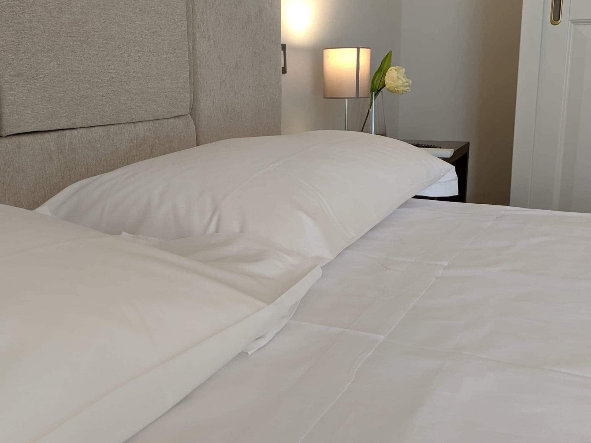 A neatly made bed with white linens and a headboard.