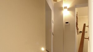 A staircase with a wooden handrail, a light fixture on the wall, and a door at the top. - Piazza Duomo Deluxe (Cecina)