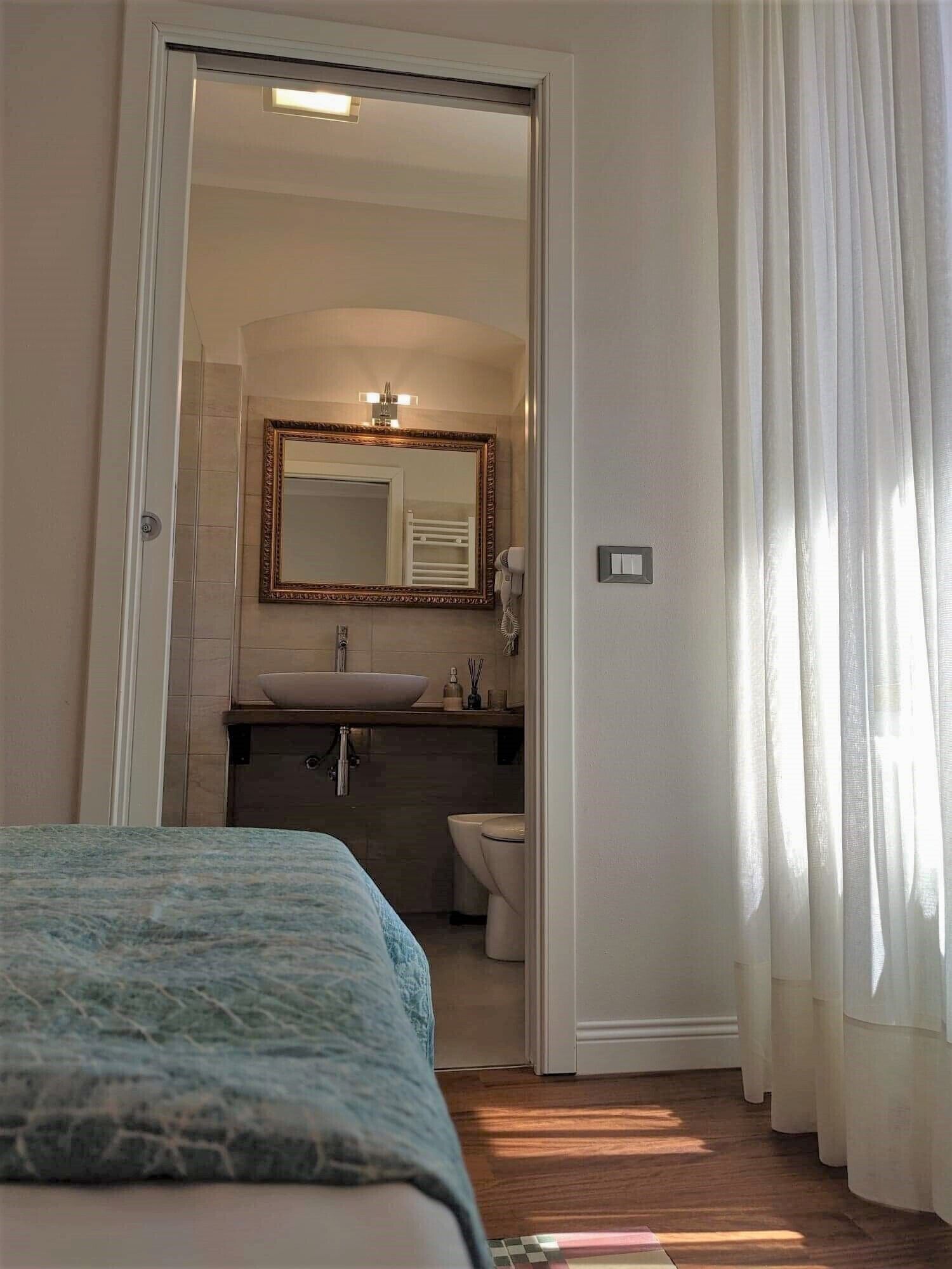 A hotel room with a bed, a bathroom with a sink, toilet, and a mirror.