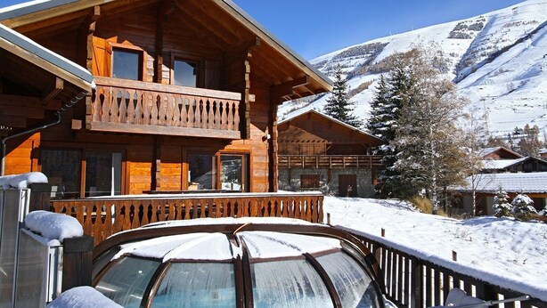 A wooden chalet with a balcony, surrounded by snow-covered mountains.