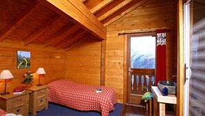 A cozy wooden cabin bedroom with a bed, bedside tables, a small desk, and a window with a view of the mountains.