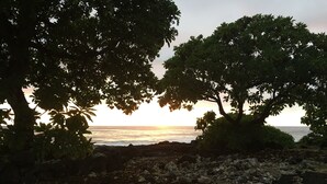 Uma linha costeira rochosa com árvores emoldurando a vista do oceano ao pôr do sol.