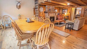 A rustic interior with a wooden dining table surrounded by chairs, a stone fireplace, and a cozy seating area with a sofa and armchairs. - Epic McCall Group Cabin | Close to Park, Lake,Town (McCall)