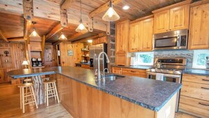 A kitchen with wooden cabinets, a large island with stools, stainless steel appliances, and pendant lighting. - Epic McCall Group Cabin | Close to Park, Lake,Town (McCall)