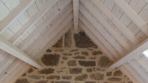 A bedroom with a stone wall, wooden beams, and a white bedspread.