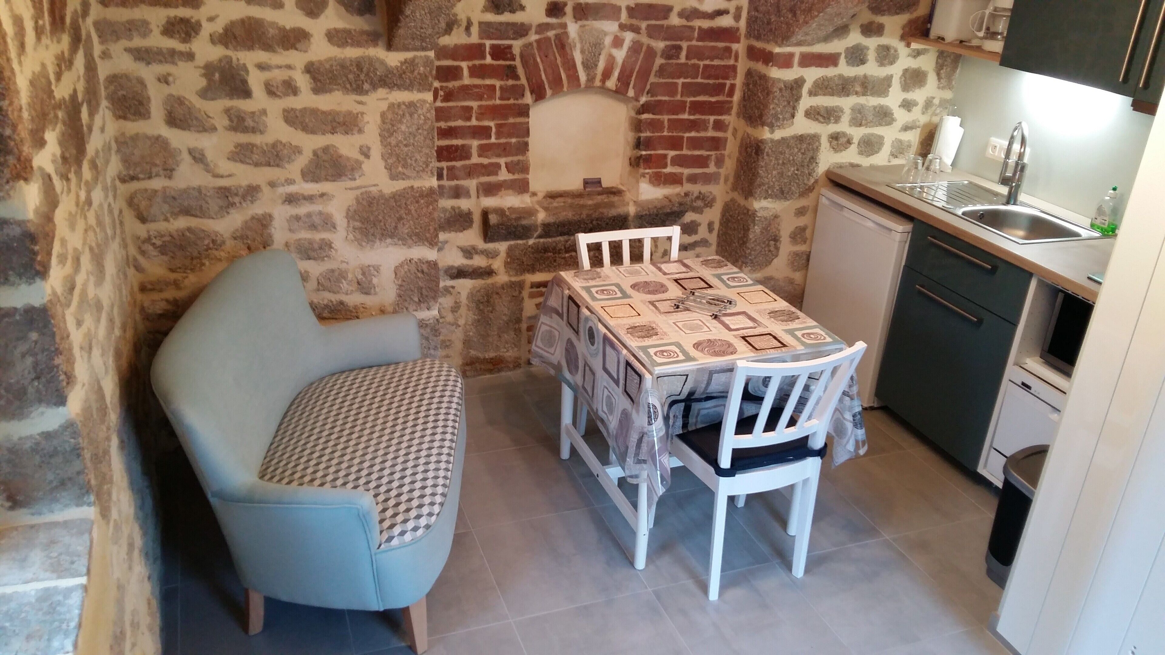 A compact kitchen with a stone wall, a small dining table with chairs, and a built-in oven.