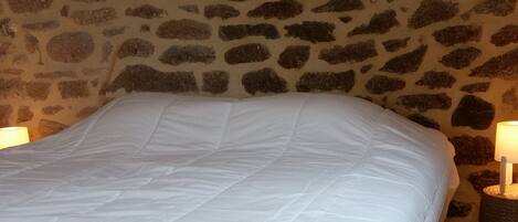 A bedroom with a stone wall, a wooden ceiling, and a bed with white bedding.