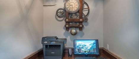 Een houten bureau met een Brother printer, een Acer monitor en een mechanisch klokje.