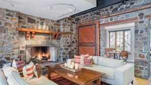 Una sala de estar acogedora con pared de piedra, chimenea, sofá blanco y mesa de centro de madera.