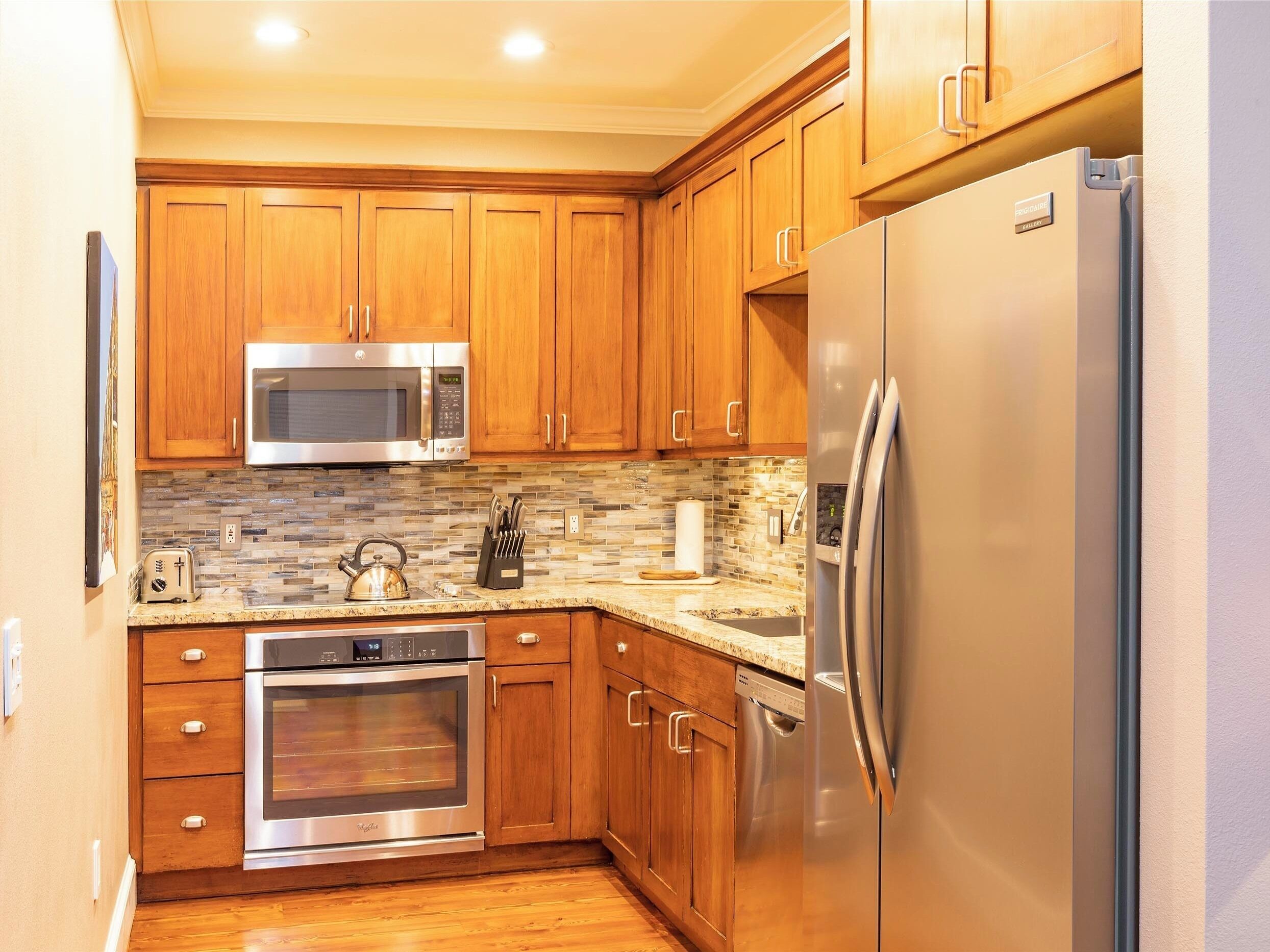Una cocina con armarios de madera, un refrigerador de acero inoxidable, un microondas, un tostador y un horno.