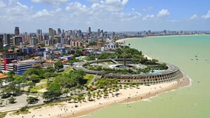 Un paysage urbain côtier avec un imposant complexe de bâtiments circulaires situé près de la plage, entouré de gratte-ciel et sous un ciel dégagé.