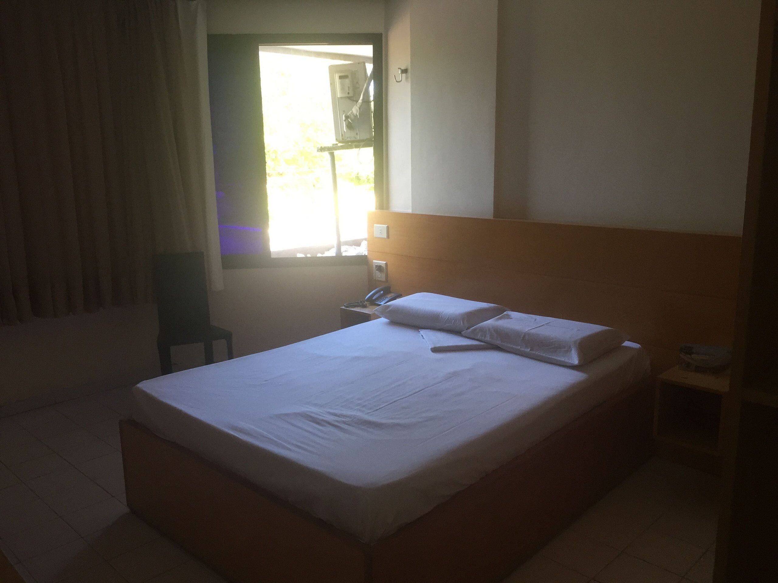 A hotel room with a bed, a desk, a chair, and a window with curtains.