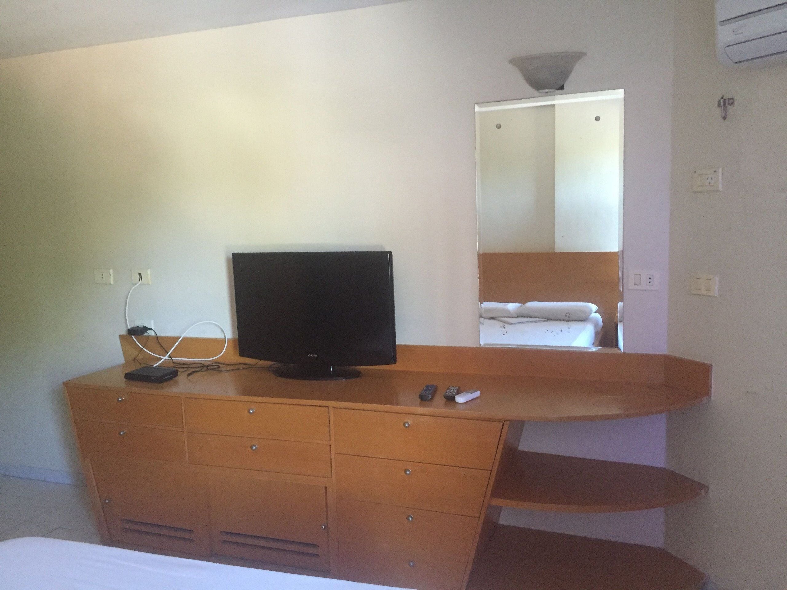 Una camera d'albergo con un comò in legno, una televisione a schermo piatto, un letto e uno specchio.