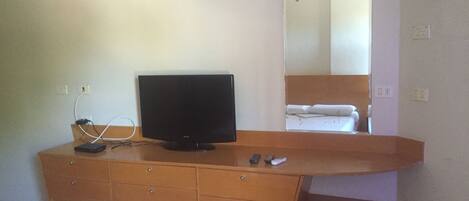 Una camera d'albergo con un comò in legno, una televisione a schermo piatto, un letto e uno specchio.