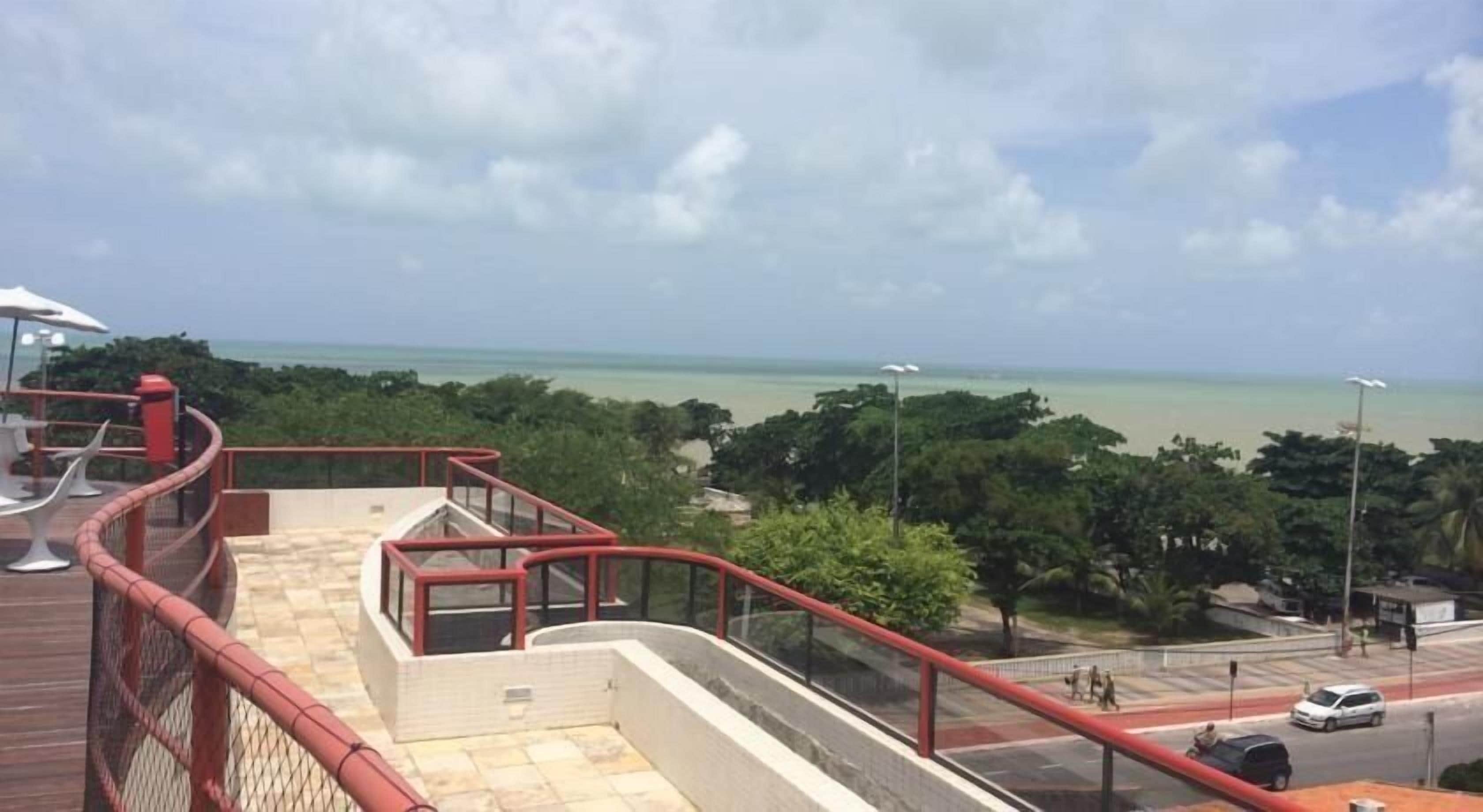 Un balcon avec vue sur l’océan et une route où circulent des véhicules.