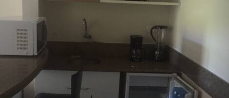 A compact kitchen with a microwave, a blender, and a refrigerator.
