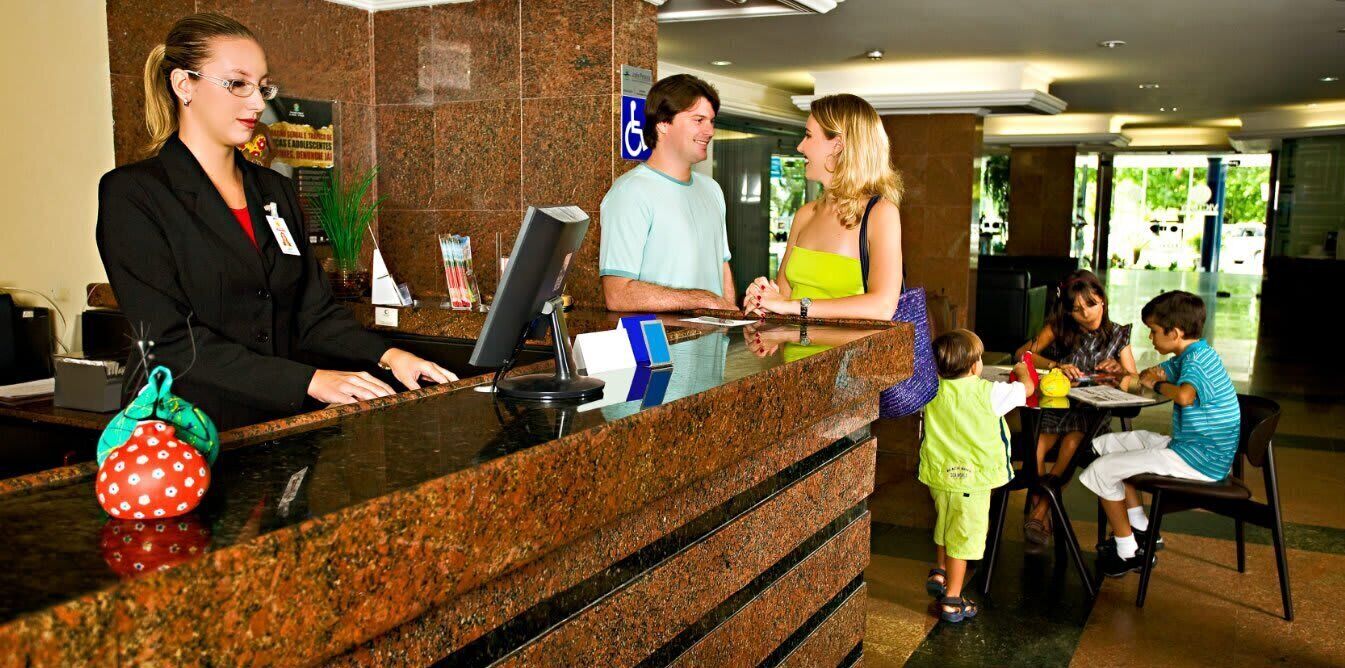 Zona de recepció d'hotel amb un recepcionista, un home i una dona al mostrador, i un nen assegut a una taula.