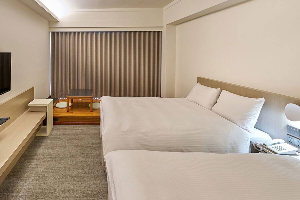 Ein Hotelzimmer mit Bett, Nachttisch, Fernseher und einer kleinen Sitzecke mit Tisch und Stühlen.