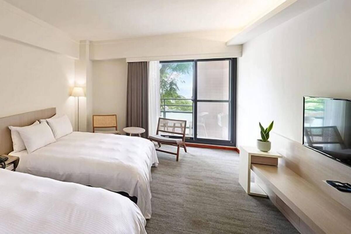 Ein Hotelzimmer mit zwei Betten, einem Fernseher, einem kleinen Tisch, einem Stuhl und einem Balkon mit Aussicht.