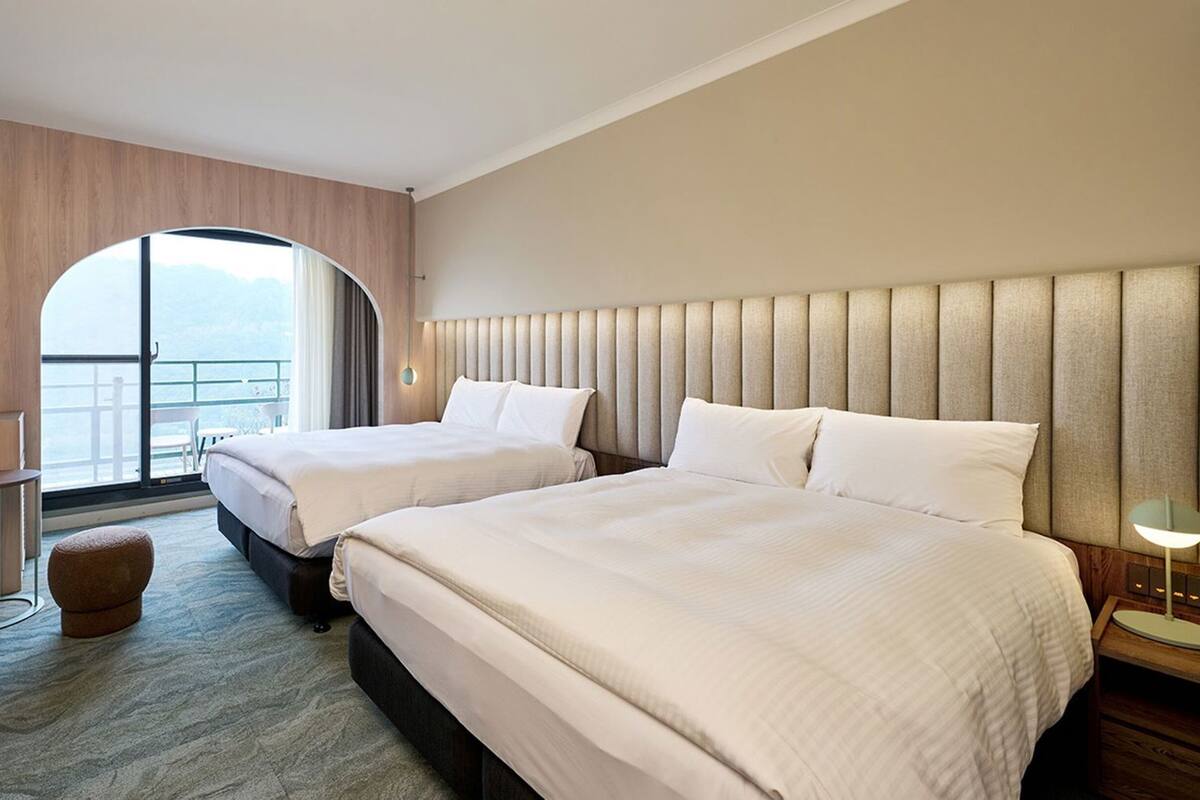 Ein Hotelzimmer mit zwei Betten, einem Fernseher, einem kleinen Tisch, einem Sofa und Blick ins Freie.
