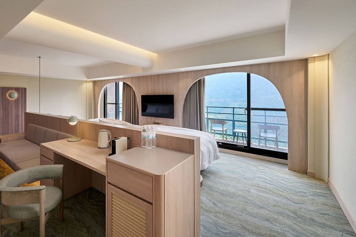 Ein modernes Hotelzimmer mit Schreibtisch, Sitzecke und großem Fenster mit Blick.
