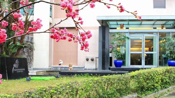 A building with a glass entrance, a stone wall, and a flower branch in the foreground. - Howard Lake Resort Shihmen Dam (Taoyuan City)