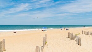 A beach with a wooden fence, a few umbrellas, and a few people. - Saltaire Cottage 11: 3BR Steps to Private Beach Access Screened Porch Pool (Kitty Hawk)