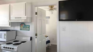 A kitchen with white cabinets, a microwave, a stove, and a black TV mounted on the wall. - Saltaire Cottages8: 2BR Ocean View Steps2 Private Beach Access Screen Porch Pool (Kitty Hawk)