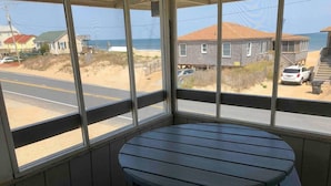 A corner room with a round table and bench, large windows with a view of the beach and houses. - Saltaire Cottages8: 2BR Ocean View Steps2 Private Beach Access Screen Porch Pool (Kitty Hawk)