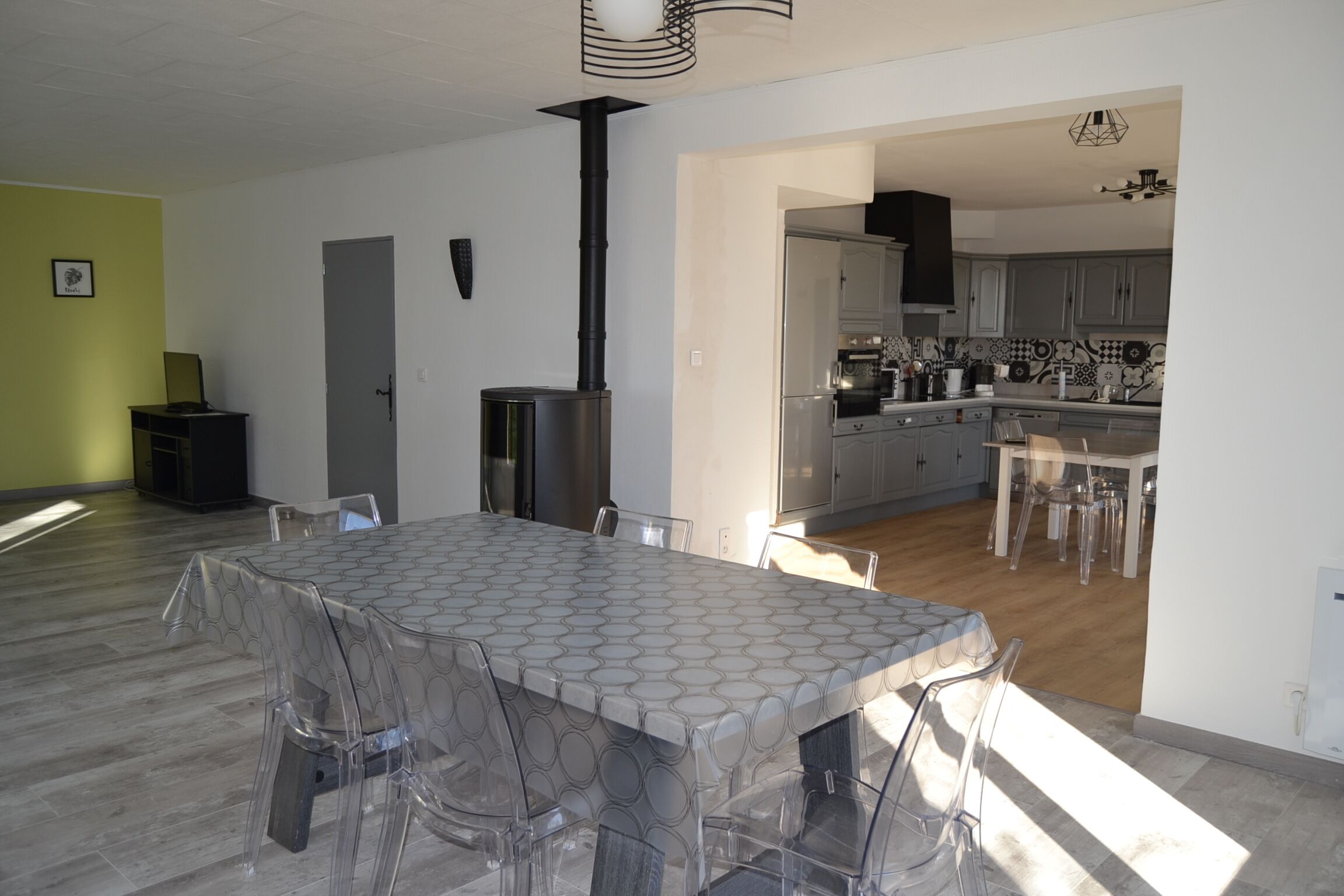A modern kitchen with grey cabinets, a black stove, and a dining area with a glass table and chairs.