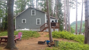 A cabin with a deck, surrounded by trees and a dirt path. - Waterfront cottage on Lake Christopher, screened in porch w/ lake views, firepit (WOODSTOCK)