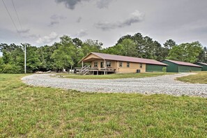 A two-story house with a porch, a gravel driveway, and a green building in the background. - The Aviator at Kudzu Cove Cabins Resort (Guntersville)