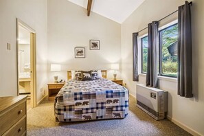 Ein Schlafzimmer mit einem Bett, Nachttischen, einem Fenster mit Vorhängen und einem Heizkörper.