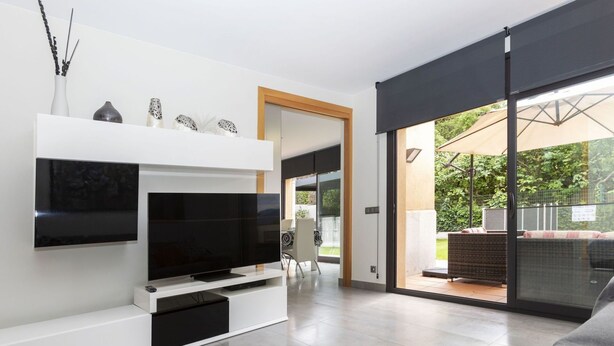 Uma sala de estar moderna com uma TV de tela plana, um sofá e uma porta de vidro deslizante que dá para um pátio externo.