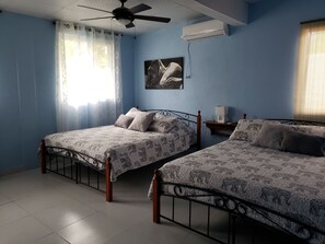 A bedroom with two beds, a ceiling fan, an air conditioner, and a window with curtains. - Pink Palace Panama (Punta Chame)