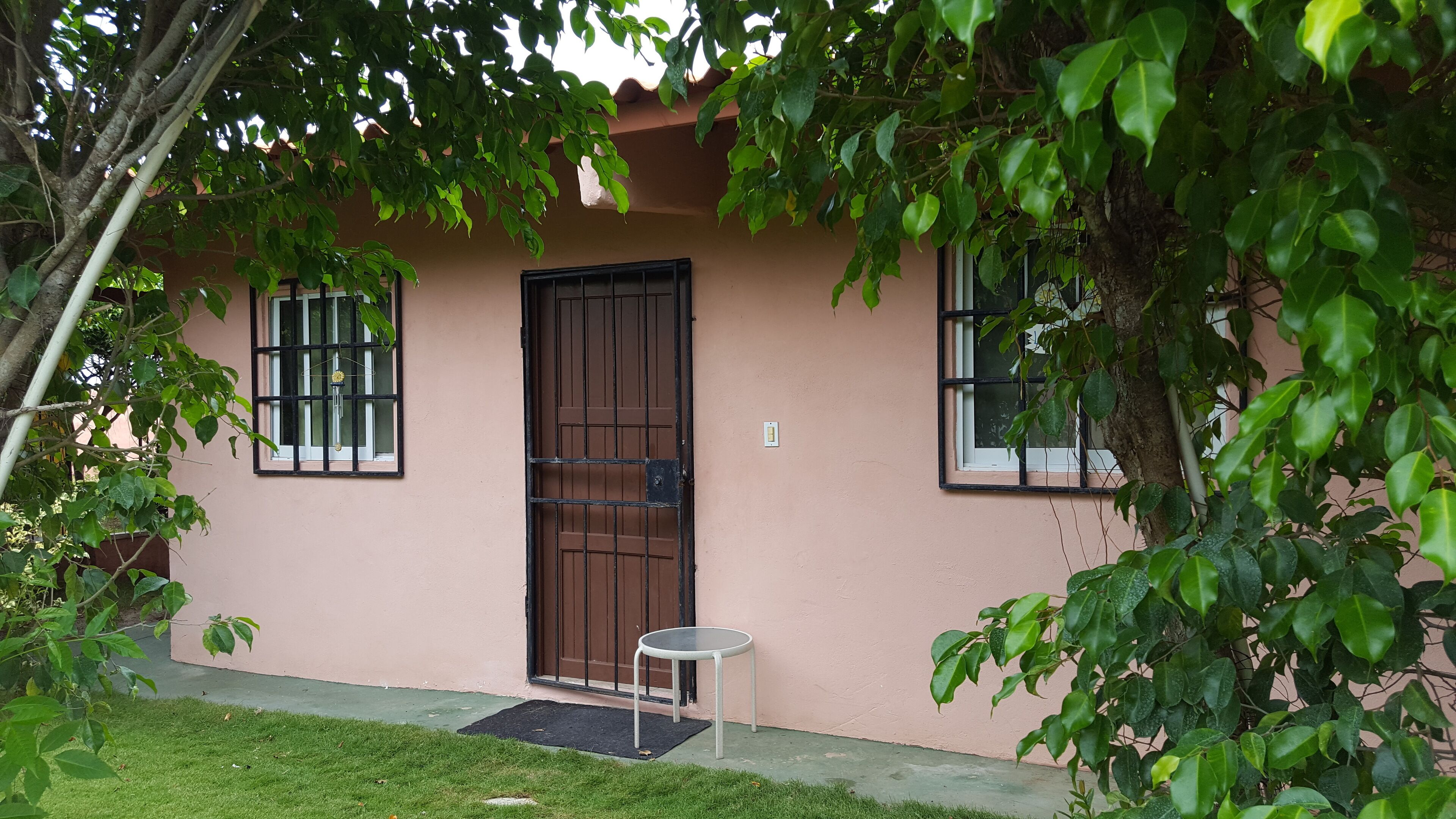 A house with a brown door, two windows with black bars, and a small round table outside.