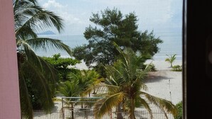 A balcony with a table and chairs, a palm tree, and a view of the beach. - Pink Palace Panama (Punta Chame)