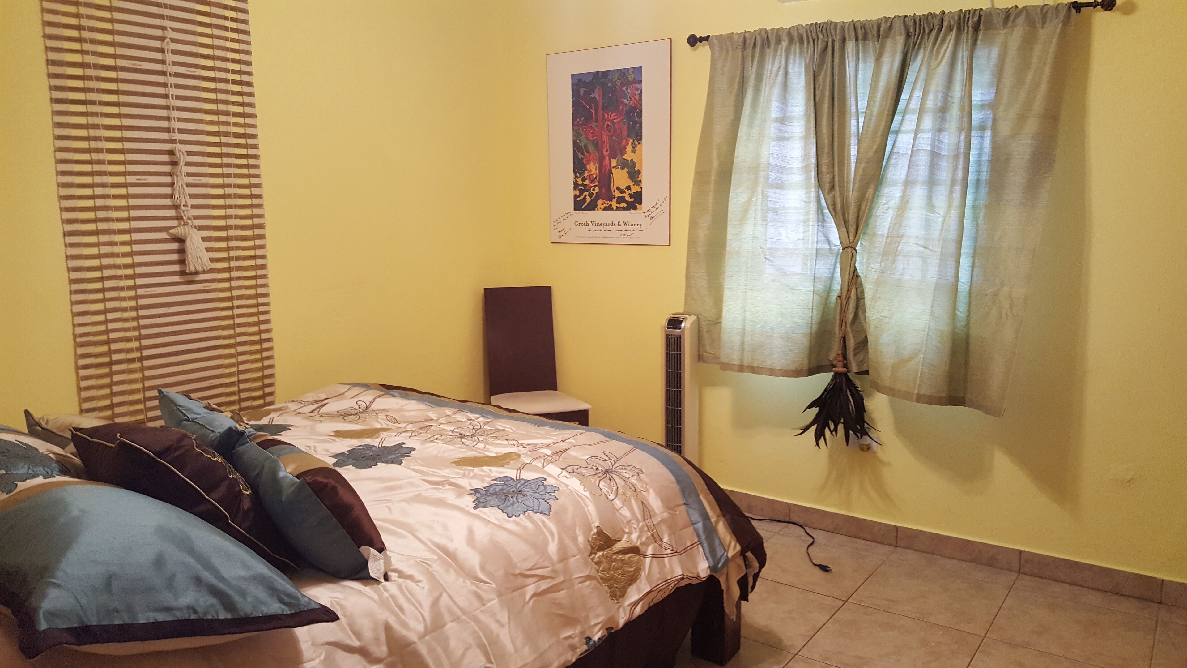 A bedroom with a bed, a chair, a poster on the wall, and a window with curtains.