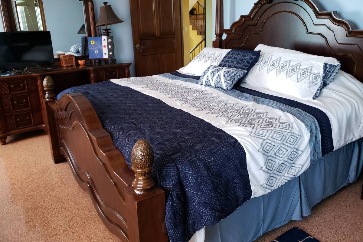 Una cama bien hecha con una colcha estampada y almohadas, un cabecero de madera y un aparador con espejo y lámpara.